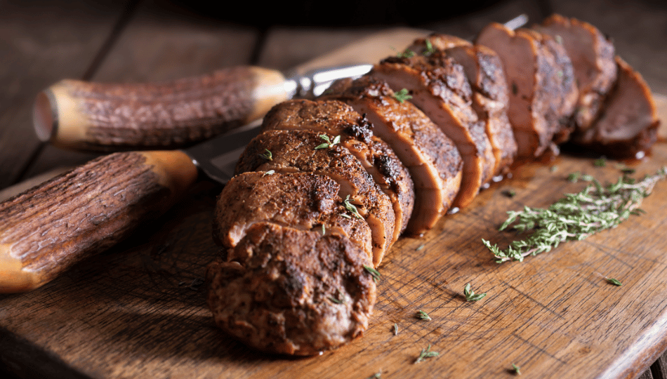 Saftig gegrilltes, in Scheiben geschnittenes Schweinefilet auf einem Holzbrett mit frischem Thymian – perfekt zubereitet nach dem Schweinefilet marinieren für eine krosse Kruste.